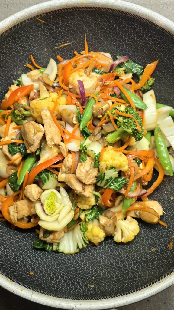 Colourful vegetable and chicken stir fry cooking in a wok on the stovetop.