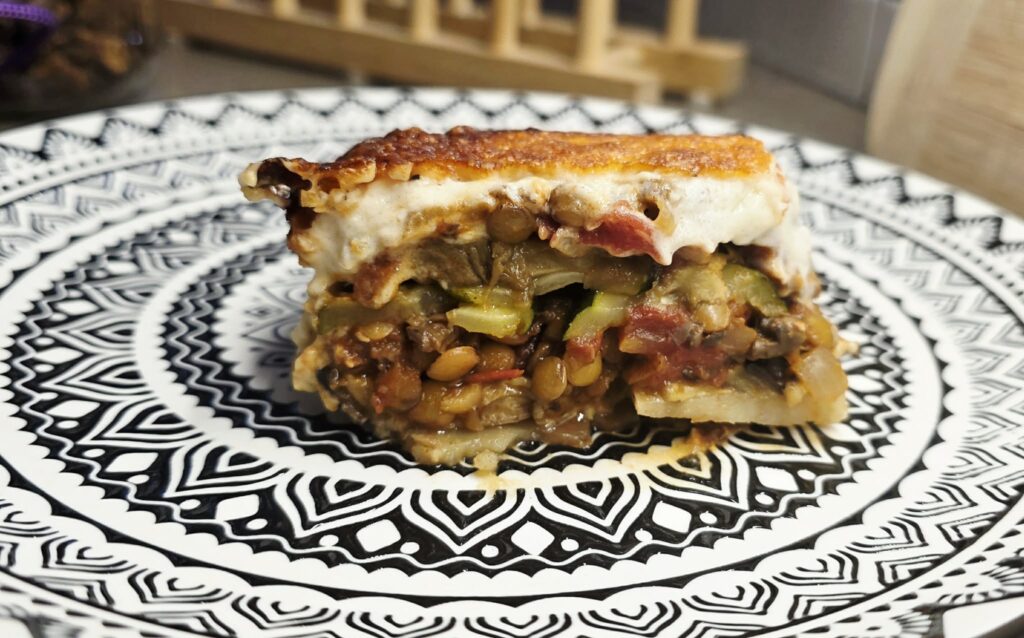 Slice of vegetarian lentil moussaka served on a plate showing layered vegetables and béchamel