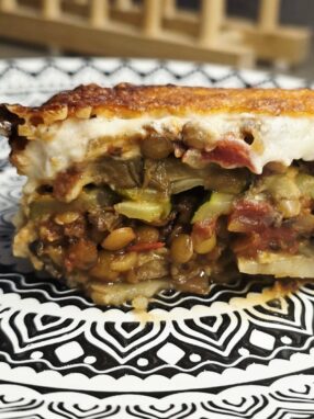 Slice of vegetarian lentil moussaka served on a plate showing layered vegetables and béchamel