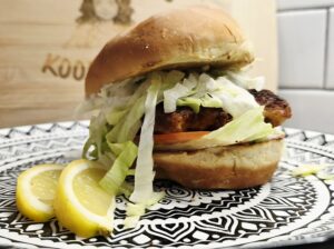 Close-up of crispy fish sandwich with garlic herb sauce and lemon wedges on a plate