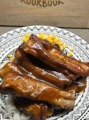 Sweet and sour spare ribs served over rice with corn, coated in a glossy homemade sauce