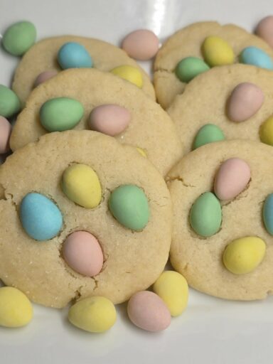 Close-up of soft mini eggs sugar cookies topped with pastel chocolate eggs, showing a soft and chewy texture