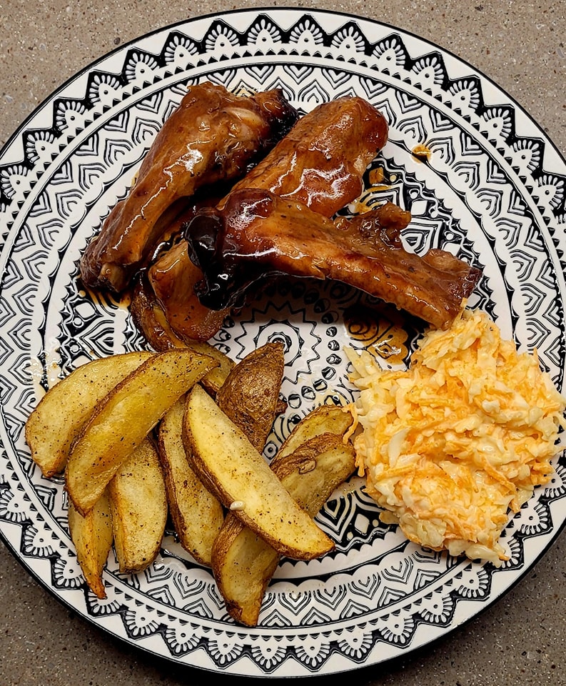 Sweet and sour ribs served with seasoned potato wedges and creamy coleslaw